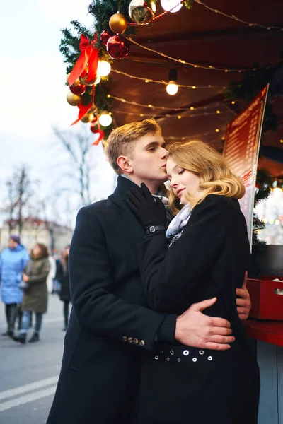 Elegante pareja romántica con estilo en el abrazo de amor, el hombre abrazando y besando a su novia con brillantes decoraciones de fondo festivas rojas.. —  Fotos de Stock
