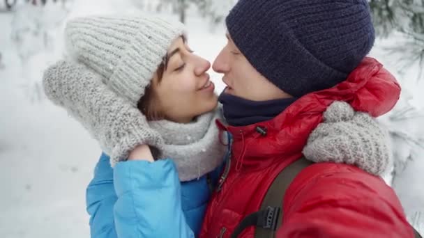 Крупный план портрета счастливой улыбающейся молодой пары, гуляющей в снежном зимнем парке в холодный зимний день. мужчина и женщина прекрасные объятия поцелуи и смех . — стоковое видео