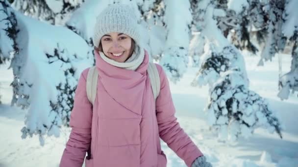 スローモーション美しい笑顔の若い女性で暖かいピンクのパーカー歩く雪の冬の公園でfrozzy晴れた日 — ストック動画