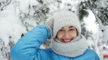 Sıcak yün şapkalı ve uzun atkılı neşeli genç bir kadının karlı kış parkında dikilen portresi.