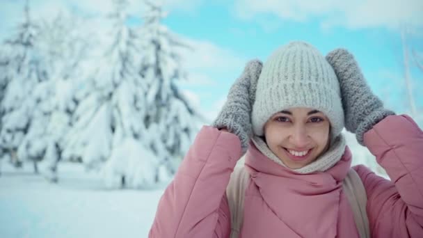 雪の冬の森の中でポーズをとっている暖かいピンクのパーカーの愛らしい笑顔の女の子の肖像 — ストック動画