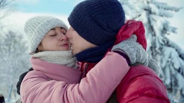 晴れた冬の日に雪の冬の公園を歩いている間に幸せな笑顔のカップルのキスと抱擁のクローズアップ肖像画. — ストック動画