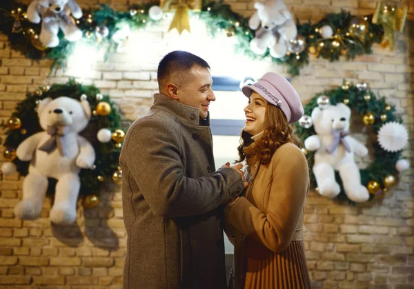 romantic stylish couple in warm clothes embracing, smiling and touching each other on festive decorations background.