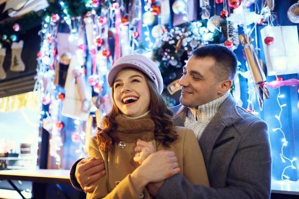 Pareja romántica y elegante con ropa cálida reír, divertirse y sentirse feliz, levantarse contra las brillantes decoraciones navideñas.. —  Fotos de Stock