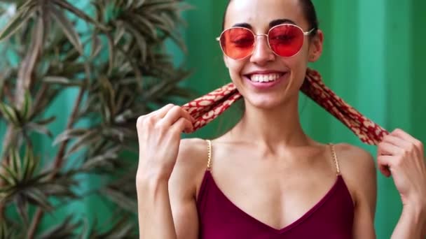 Hermosa joven alegre en un vestido ligero borgoña posando sobre fondo de pared verde — Vídeo de stock