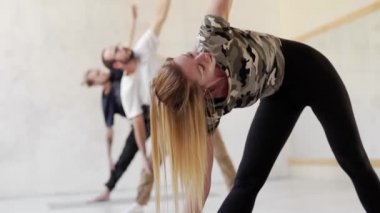 İçeride yoga yapan bir grup genç sporcu. Önplandaki çekici sarışın kadın.