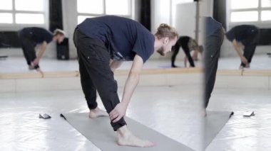 Ağır çekim yakışıklı adam hafif yoga sınıfında yoga yapıyor.