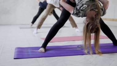 Yoga sınıfındaki genç insanlar yavaş çekimde yoga yapıyor ve bacak ve sırt egzersizleri yapıyorlar..