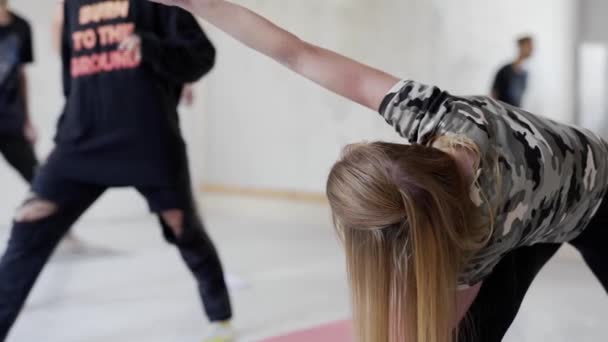 Grupp av unga sportiga människor som utövar yoga inomhus. attraktiv blond kvinna på förgrunden — Stockvideo