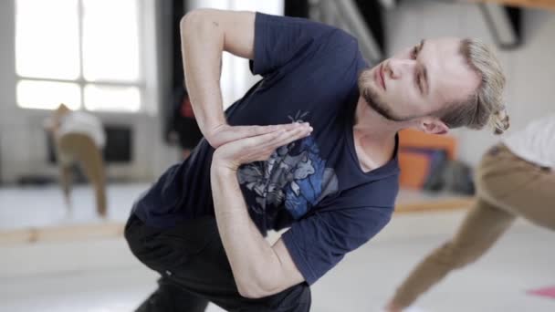 Gruppe junger Sportler, die Yoga im Innenraum praktizieren. schöner Mann im Vordergrund. — Stockvideo