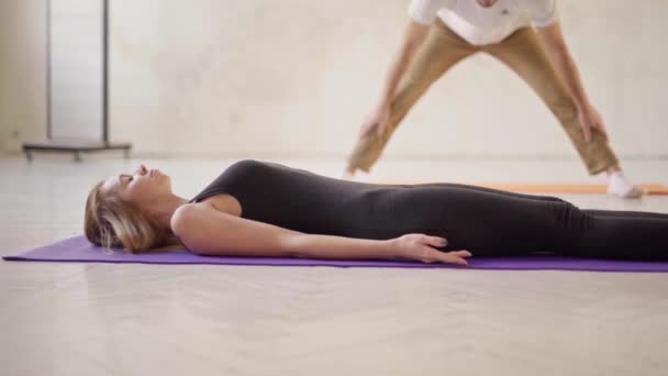 Вид сбоку спортивная расслабленная женщина практикующая йогу в классе йоги, лежащая в покоящейся позе Savasana или Dead Body упражнения в студии йоги белого цвета — стоковое видео