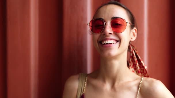 Close up bela sorridente jovem mulher em sundress leve e óculos rosa posando no fundo da parede vermelha — Vídeo de Stock