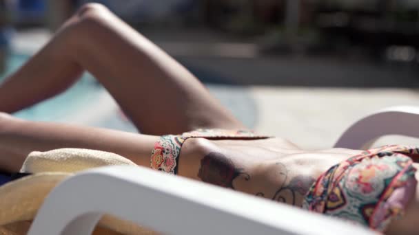 Όμορφη γυναίκα λευκό μπικίνι με σώμα και επίπεδη κοιλιά ξαπλωμένη στην άκρη της πισίνας σε καρέκλα γραφείου και ηλιοθεραπεία — Αρχείο Βίντεο