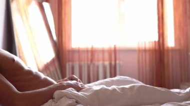 Yorgun ve uykulu genç adam yatakta uyanıyor, kalkıyor ve arkasına yaslanıyor.