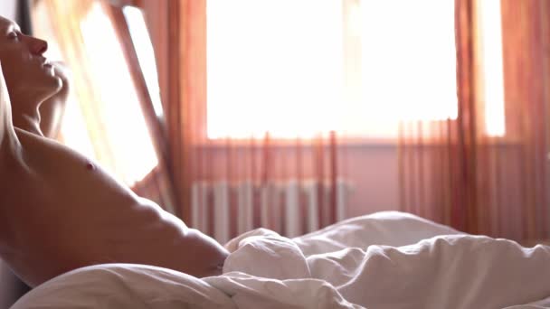 Schöner junger Mann schläft gemütlich im Bett, wacht morgens auf und dehnt sich faul — Stockvideo