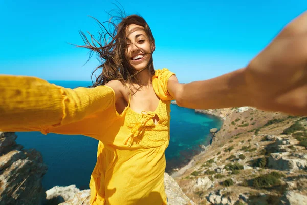 Mutlu, bronz tenli kadın özçekim yapıyor ve uçurumun kenarındaki güzel deniz manzaralı kameraya gülümsüyor.. — Stok fotoğraf