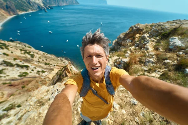 Young male tourist making selfie and smile to the camera on cliff edge with beautiful sea view and enjoying wonderful nature. — Stock Photo, Image