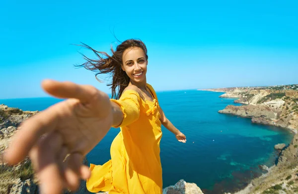Gelukkige mooie gebruinde vrouw staande op klif rand met prachtig uitzicht op zee. hand reiken, volg mij — Stockfoto