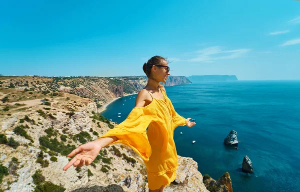 Šťastná atraktivní opálená žena pózující s roztaženými pažemi na okraji útesu s krásným výhledem na moře. — Stock fotografie