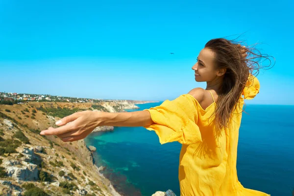Šťastná atraktivní opálená žena pózující s rukou nataženou na okraji útesu s krásným výhledem na moře. — Stock fotografie