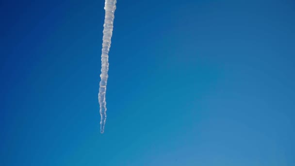 Большая длинная сосулька на фоне ярко-голубого неба — стоковое видео