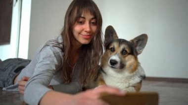 Güzel genç bir kız sevimli, meraklı Corgi köpeğine sarılıp öpüyor ve selfie çekiyor.