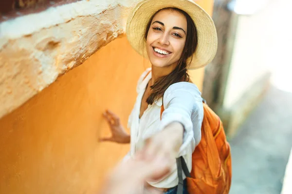 Feliz mujer turista despreocupada en sombrero de paja, camisa blanca y mochila naranja de la mano de su novio, sígueme . — Foto de Stock