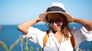Yavaş çekim çekici, mutlu kız turist hasır şapka ve gözlük güneşli bir günde deniz kenarında poz veriyor.