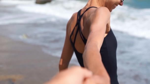 Unga par håller händer flicka ledande pojkvän promenader mot vackra soliga vågiga stranden — Stockvideo