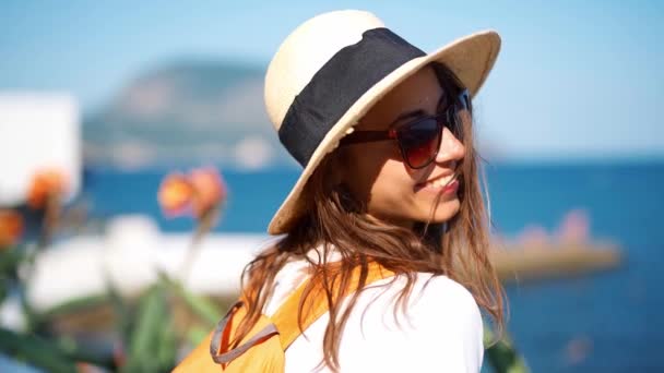 Крупный план замедленной съемки очаровательная улыбающаяся женщина путешественница в соломенной шляпе и солнцезащитных очках прогуливаясь по морю в солнечный день — стоковое видео