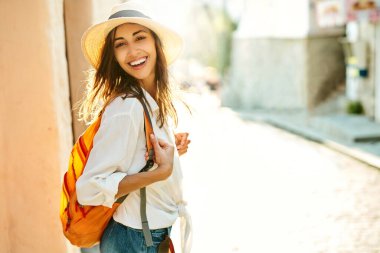 Eski caddede yürüyen neşeli turist kadın, kameraya doğru dönüyor.