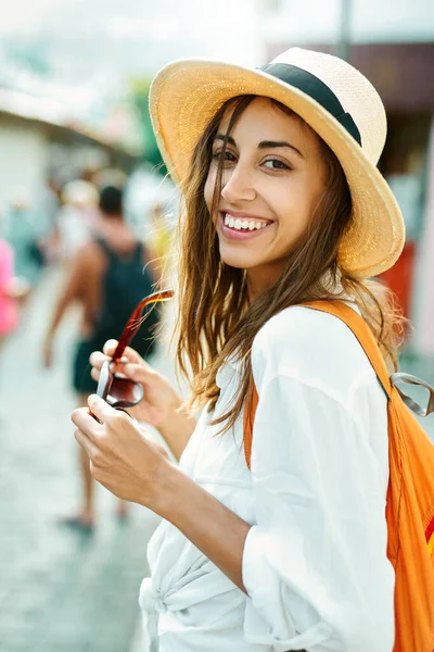 Портрет крупным планом радостной туристки в соломенной шляпе и белой рубашке, смотрящей в камеру с улыбкой . — стоковое фото