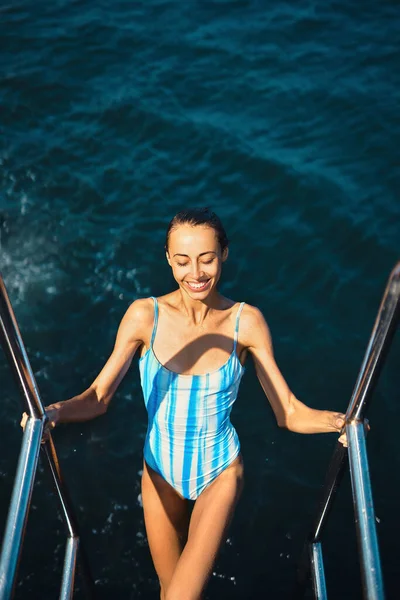 Bella donna felice sexy snella in costume da bagno blu esce dal mare, in una calda giornata estiva soleggiata . — Foto Stock