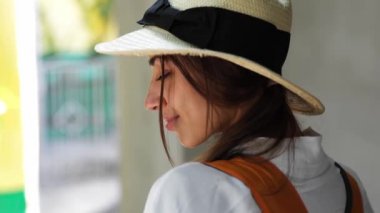 Yakın plan portre, beyaz gömlekli beyaz şapkalı beyaz kadın turist beton bina duvarında duruyor.