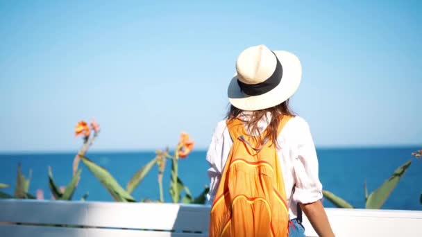 Tillbaka visa slow motion ung kvinna turist halm hatt och orange ryggsäck njuter av havsutsikt vid havet på solig dag. — Stockvideo