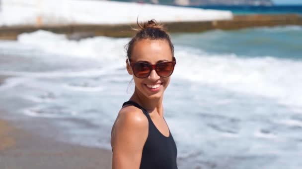 Alegre risueño mujer en traje de baño y gafas de sol invitando novio para caminar en la soleada playa de mar con olas — Vídeos de Stock