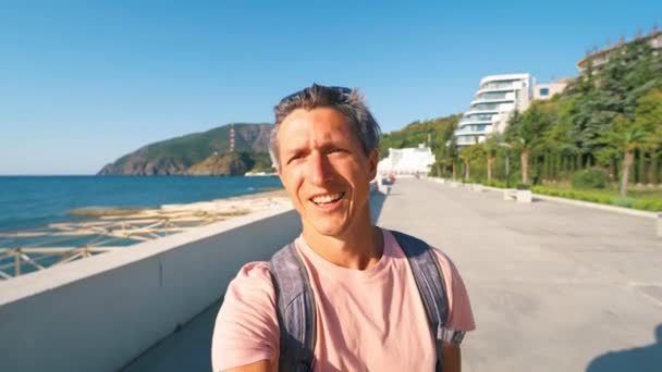 Bonito sorridente bronzeado homem viajante turista blogueiro filmar vídeo selfie na baía de beira-mar no dia ensolarado — Vídeo de Stock