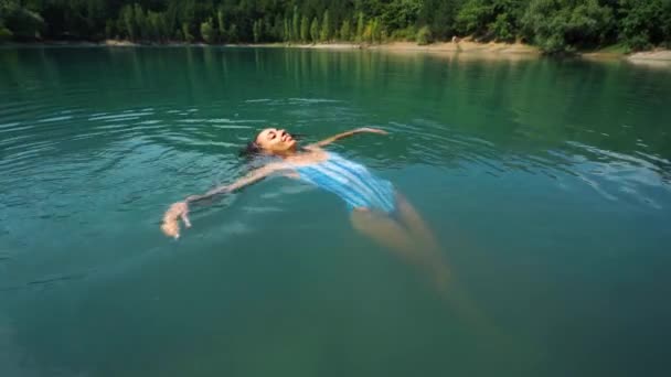 Красивая стройная счастливая женщина в голубых купальниках расслабляется, купается и наслаждается пресной водой в горном озере в жаркий солнечный летний день . — стоковое видео