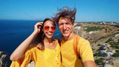 Güzel bir çift turist selfie çekiyor ve uçurumun kenarında kameralara gülümsüyor. Deniz manzarası çok güzel ve doğanın tadını çıkarıyorlar..