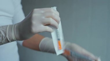 Doktor, hastanede enjeksiyon için steril şırınga açıyor. Yakın çekim elleri koruyucu steril eldivenlerle insülin şırıngasını açıyor.