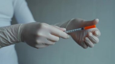 İnsülin iğnesi. Beyaz steril koruyucu eldivenli hemşire elleri şırınga iğnesinden kapağı çıkarır. Ellerinde iğne olan araç
