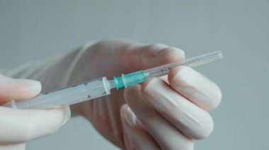 Hipodermik şırınga. Beyaz steril koruyucu eldivenli sıhhiyeci elleri şırınga iğnesinden kapağı çıkarır. Ellerinde iğne olan araç