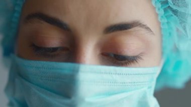 Üzgün ve yorgun doktor gözlerini açar ve kameraya bakar. Tıbbi malzeme portresi. Yakın plan. Koruyucu Yüz Maskeli Kadın, Solunum Sistemi