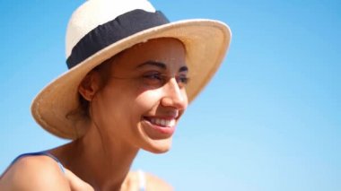 Yavaş çekim çekici, hasır şapkalı, güneşlenen ve deniz sahilinde güneşlenen bir kadın.