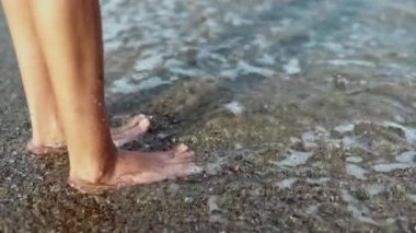 Ağır çekimde, çıplak ayakla sahilde dalgalı kadın bacakları..