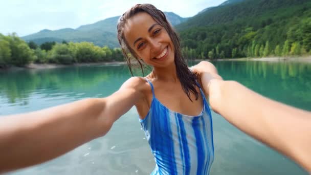Bronceada mujer sonriente en traje de baño haciendo selfie en hermoso fondo del lago de montaña — Vídeo de stock