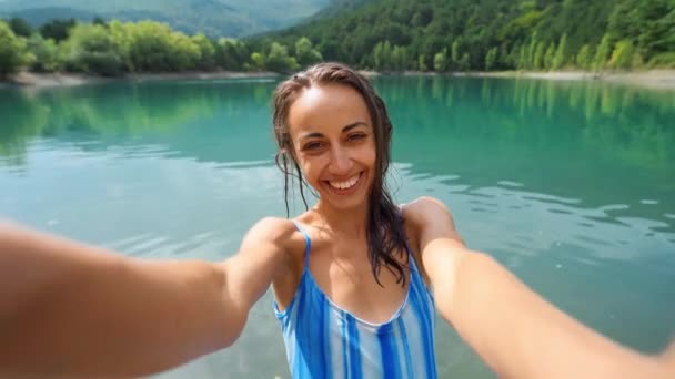 穿着蓝色泳衣的快乐的荡妇在美丽的山湖背景上自言自语 — 图库视频影像