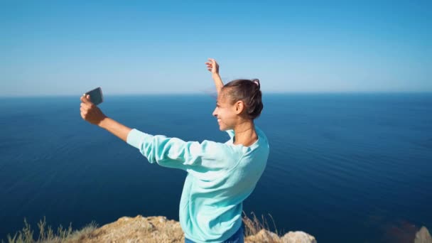 Helder portret van vrolijke lachende vrouw in felgele jurk en hoed met rugzak selfie maken op klif rand met prachtig uitzicht op zee — Stockvideo