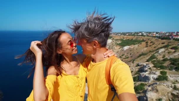 快乐可爱的一对游客穿着橙色的太阳衣和T恤衫，自拍和亲吻 — 图库视频影像