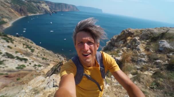 Ung man turist gör selfie och ler mot kameran på klippkanten med vacker havsutsikt och njuta av underbar natur. — Stockvideo